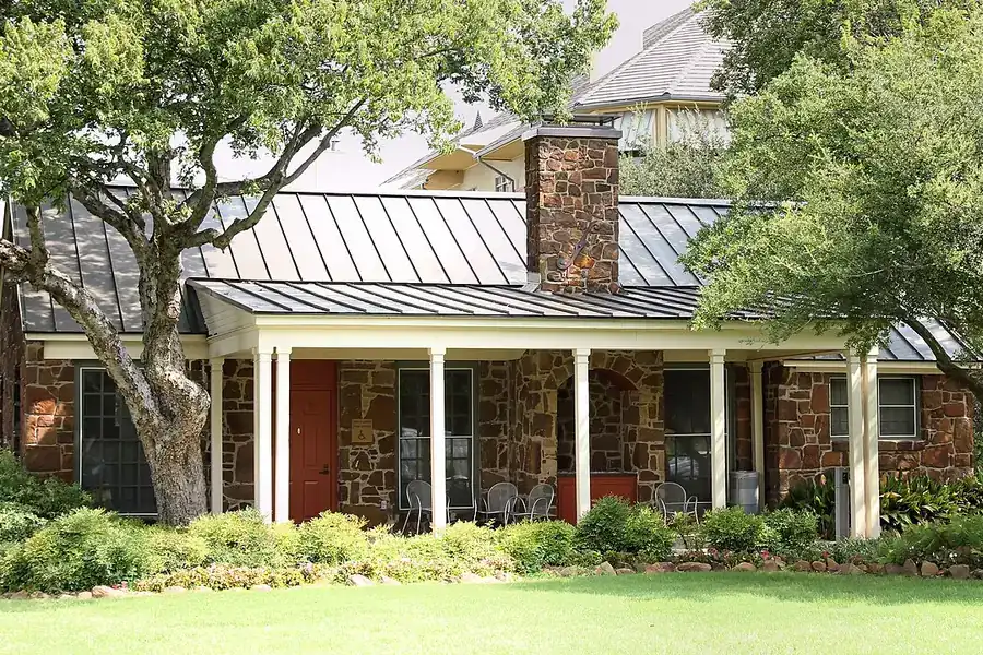 Stone Cottage, a historic stone house with a metal roof among trees in Addison, Texas