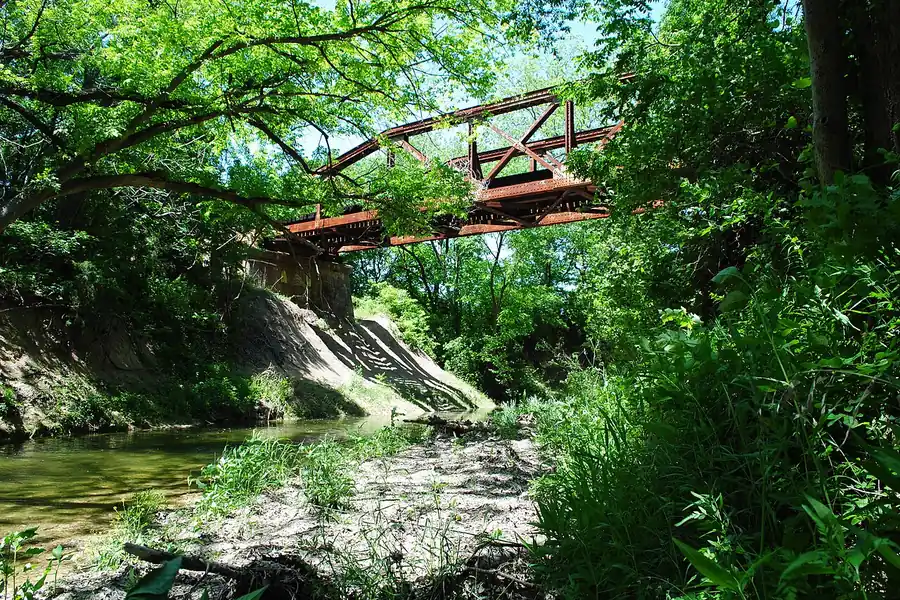 Old rusted truss railroad bridge over Red Oak Creek among green trees in Red Oak, Texas