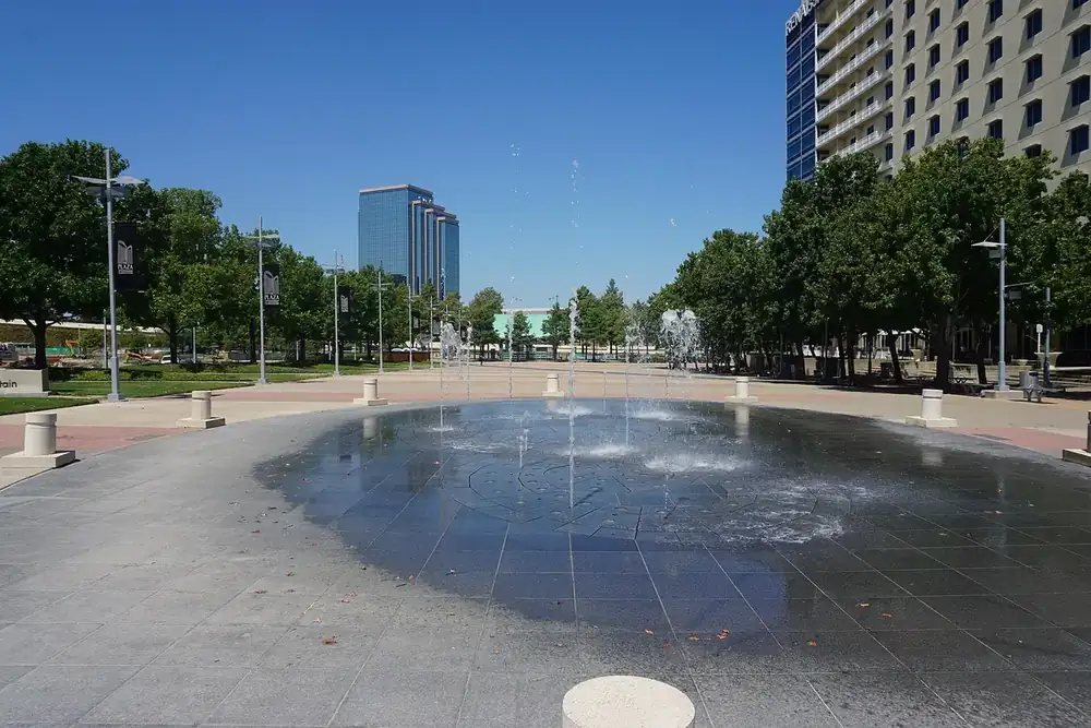 Wide plaza with a shallow splash fountain and office towers behind it in Richardson, Texas